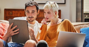 Twee personen zitten op de bank en kijken op een tablet.