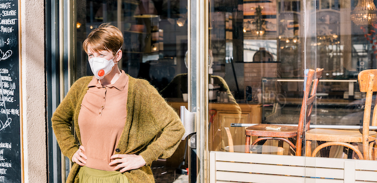 Woman standing in front of a restaurant with her hands on her hips wearing a face mask