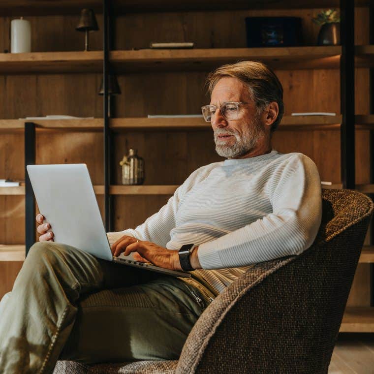 A man wearing glasses working on a laptop in a wood-panelled study