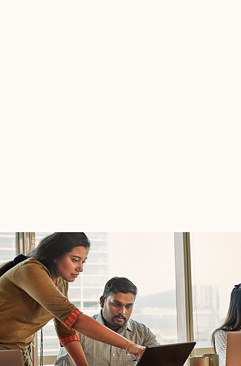 Photograph of two people looking at a computer screen. The woman is standing over the man, who is sitting at a desk with a window behind him