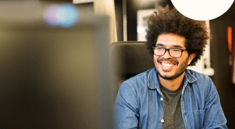 Smiling man sits behind computer screen in front of books