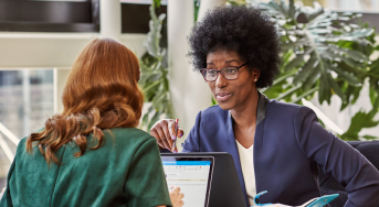 Two people sit with laptops having a conversation