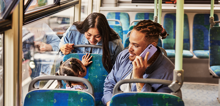 A family on a bus. One parent is taking a phone call.