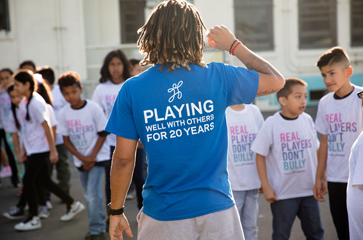 An image of a person wearing a Playworks t-shirt, surrounded by children.