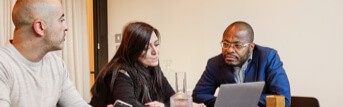 Two men and a woman speaking while sitting at a table in front of a laptop