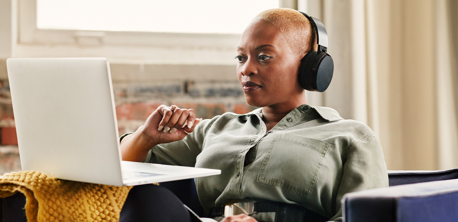 A woman sits at her laptop wearing headphones