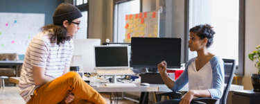 Two people working in an office environment and talking.