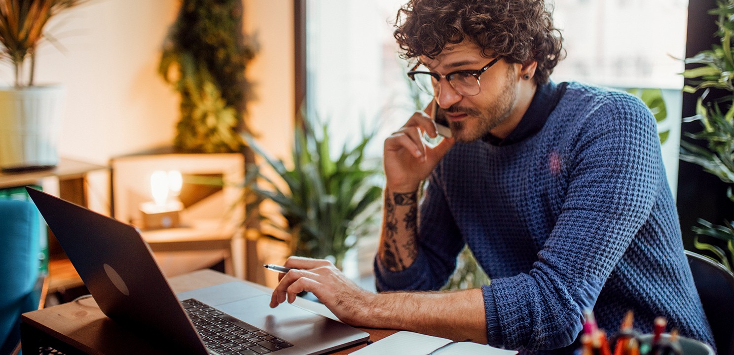 A man on the phone works in front of a laptop