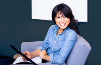A photograph of a person looking at the camera while sitting on a couch and using a tablet.