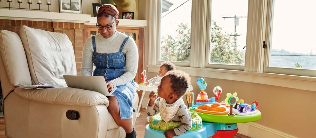 African American woman sitting on a chair in her living room with two toddlers in activity play stations.