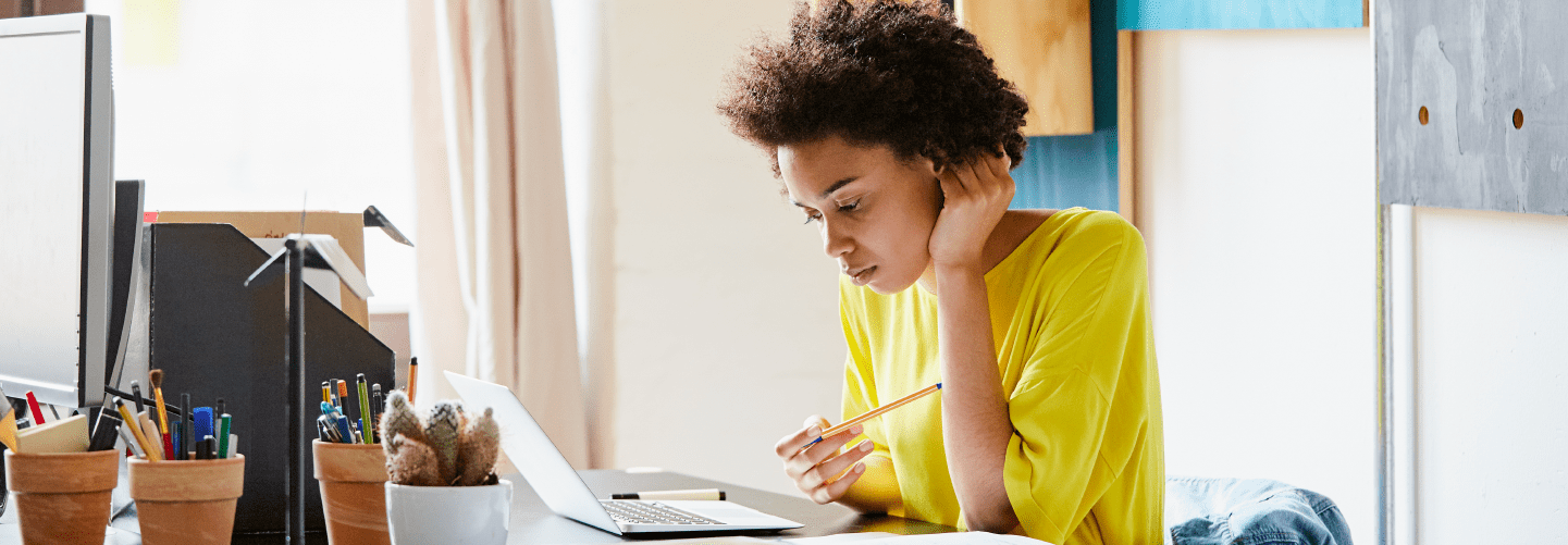 woman, wearing a yellow shirt, working on her laptop.