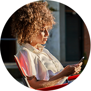 Woman with curly hair sitting in a chair and typing on a phone