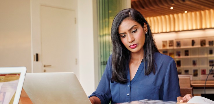Woman sitting at a desk in front of a laptop looking down at the table