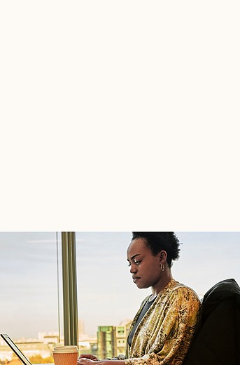 Photograph of a woman working at a desk next to a large window with a coffee cup nearby