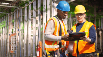 Two men in high-viz vests and hard hats consult clipboard