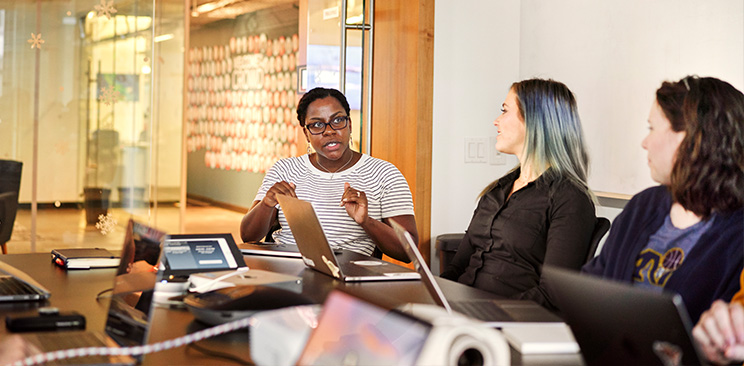 A woman speaks with her colleagues, while they look on, smiling.