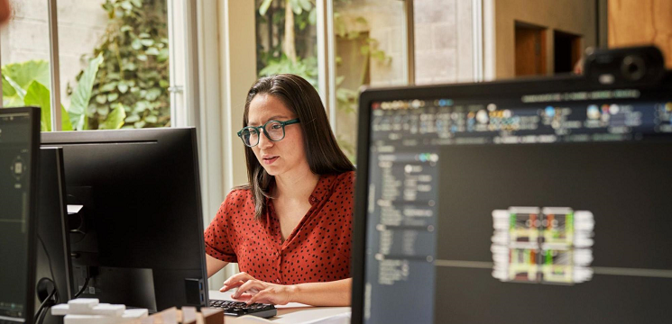 Woman wearing glasses sitting at a desk typing on a computer