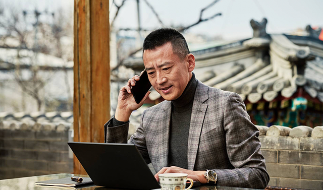 man on mobile phone while looking at laptop