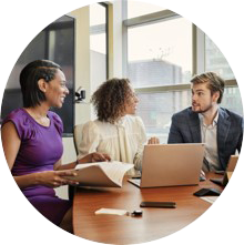 three people at a desk with a laptop, engaging in conversation