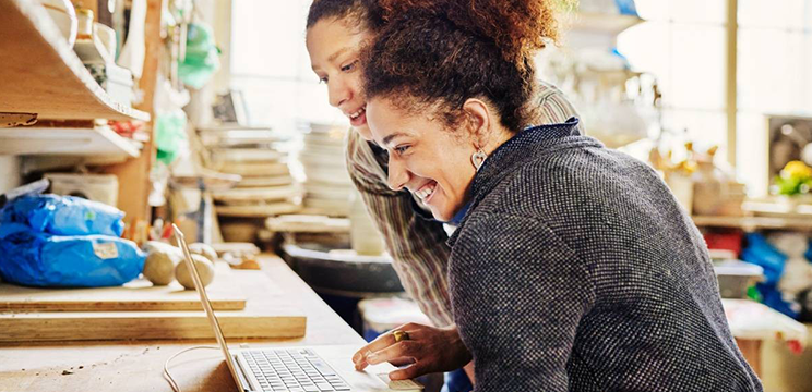 A nonprofit employee helps a coworker update their LinkedIn profile on their laptop.
