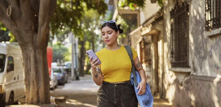 Woman walking on a sidewalk holding a mobile phone and looking down at it