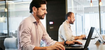 Two individuals working on their laptops at a shared desk.