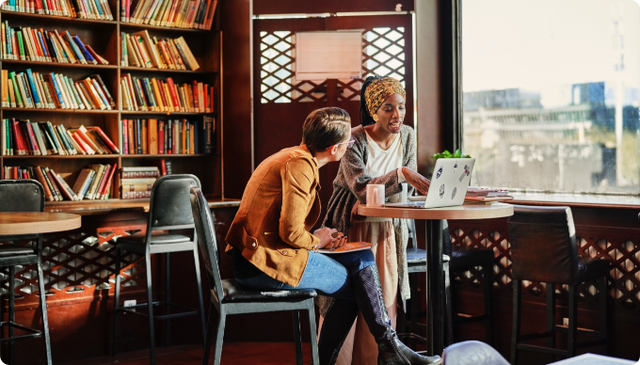 Two females seated at a table in front of a laptop conversing