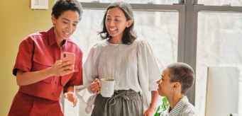 Drei Personen, die gemeinsam auf ein Smartphone schauen.