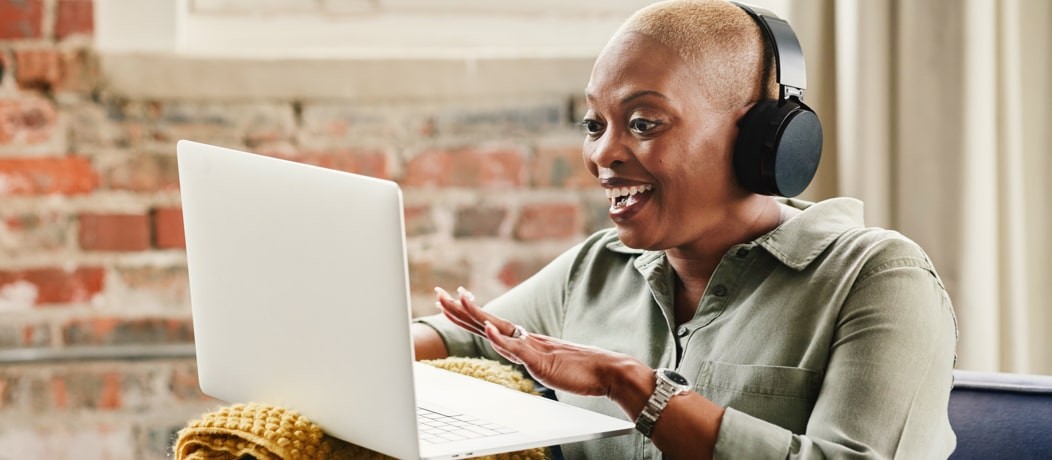 Close up of an African American woman with headphones smiling excitedly at a laptop.