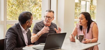 Three business-people hold a discussion at a table.