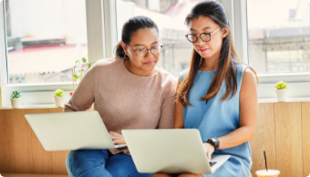 Two females each with a laptop on their laps conversing