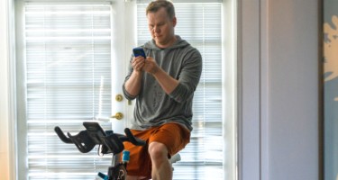 Photo of a man on an exercise bike and checking his phone.