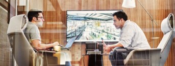 Two men sitting in chairs with laptops on their laps in front of a large TV screen