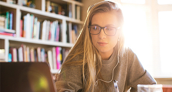 A photo of a woman working at a computer with headphones on.
