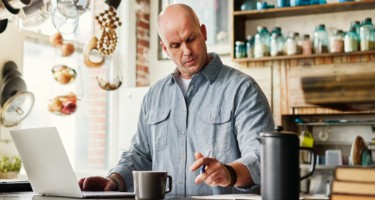 Een persoon werkt achter de laptop in de keuken.