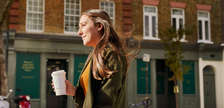 Woman walking outside down a city street with a drink in hand.