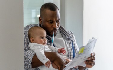 A man holds a baby with toothbrush in mouth, reading a piece of paper.
