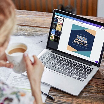 Woman holding a cup of coffee and looking at laptop screen, which reads "digital imaging specialist"
