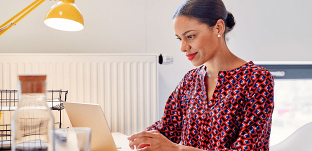 A black woman with her hair in a bun smiling down at a laptop computer.