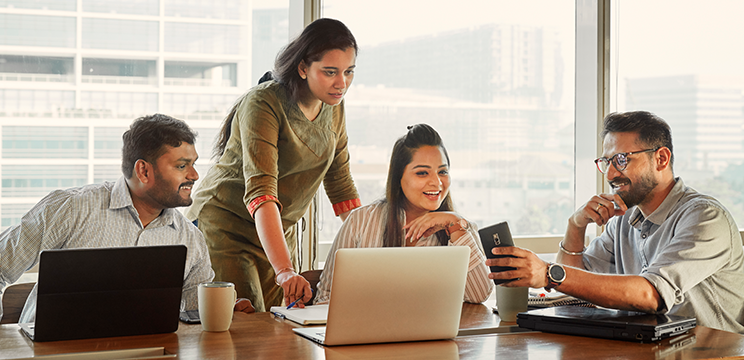Image of a team working at a table, looking at something a team member is showing them on his phone.