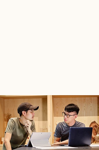 photograph of two men talking to each other at a standing table, each with their own laptop