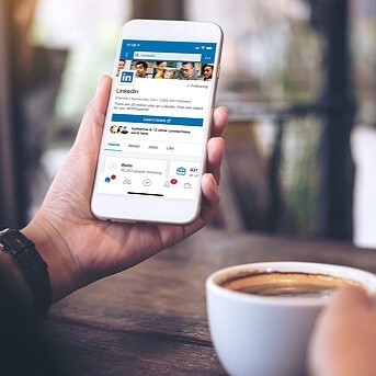 Left hand holding a phone with LinkedIn app homepage on the screen