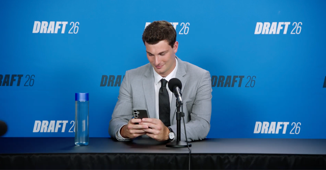 Image of man at a draft conference table, looking at his phone