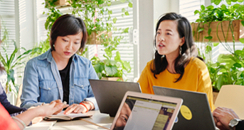 A photo of two women working at a table with houseplants in the background