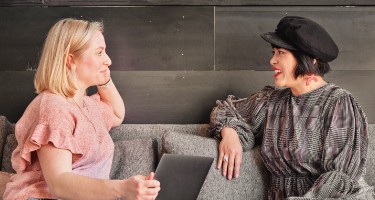 Twee personen zitten op de bank en hebben een gesprek.