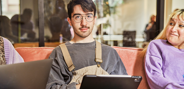 Man holding a tablet and sitting between two people in a casual office.